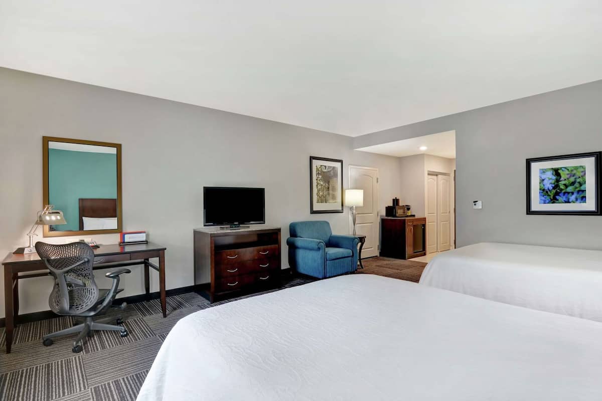 A hotel room with two beds, a desk with a computer, a chair, a TV, and a small kitchenette.