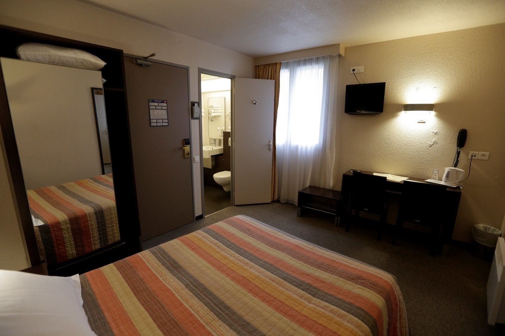 A hotel room with a bed, a desk, a television, and a bathroom visible through an open door.