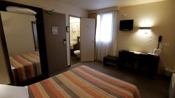 A hotel room with a bed, a desk, a television, and a bathroom visible through an open door.
