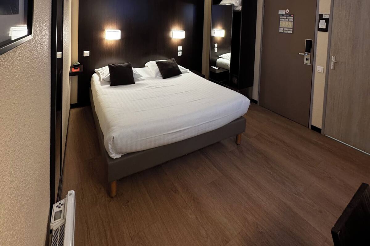Een hotelkamer met een groot bed, nachtkastjes, een spiegel en een airconditioning.