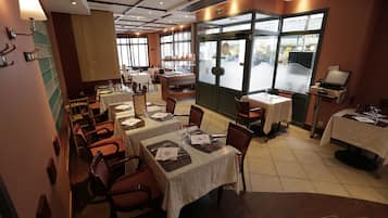 A restaurant with multiple tables and chairs, a counter with a display, and a view through a large window.