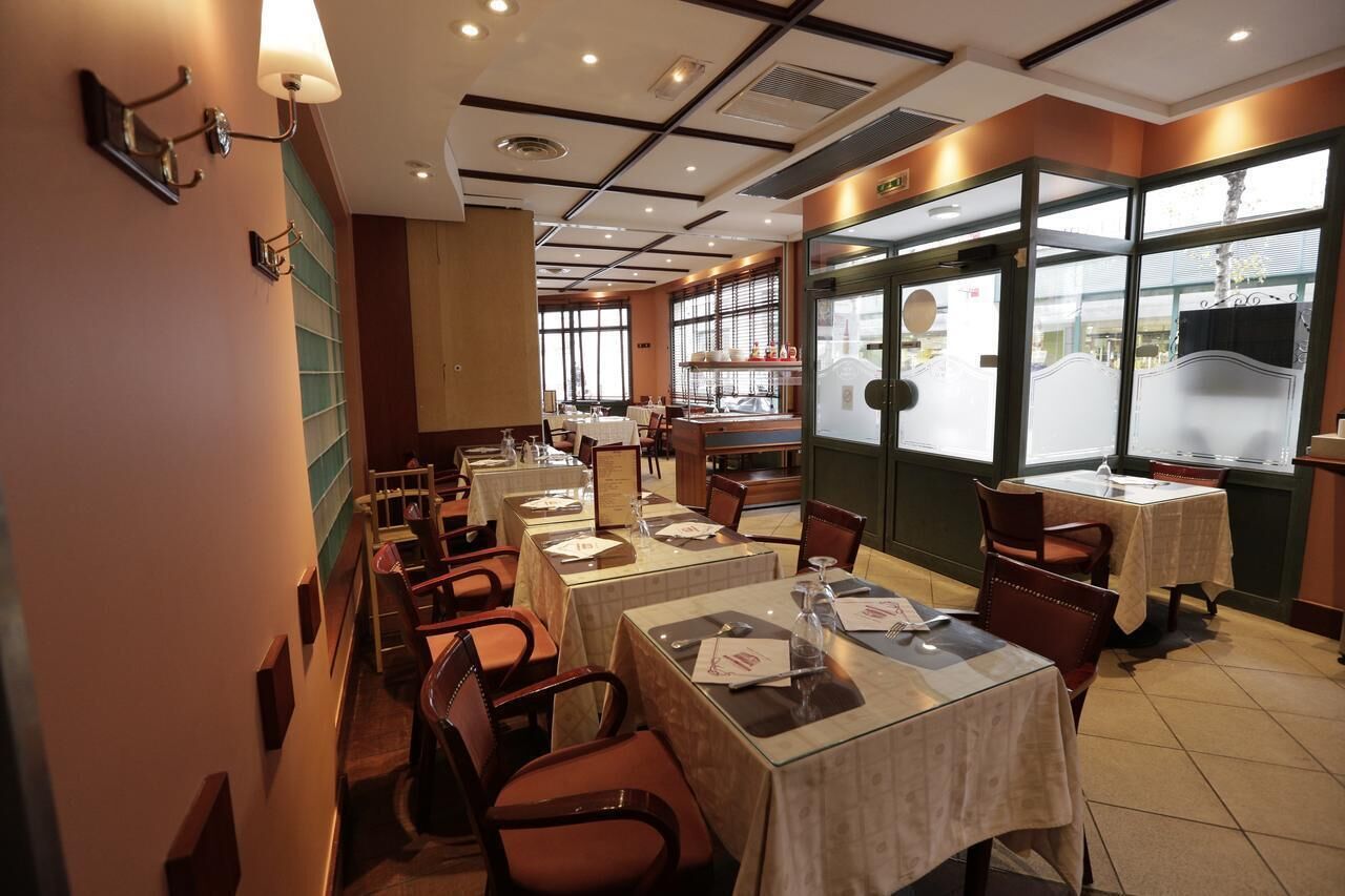 A restaurant interior with tables and chairs, a counter, and large windows.