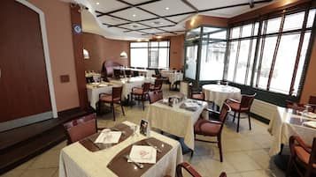 Un restaurante con varias mesas y sillas, un muro de ladrillo y amplios ventanales.
