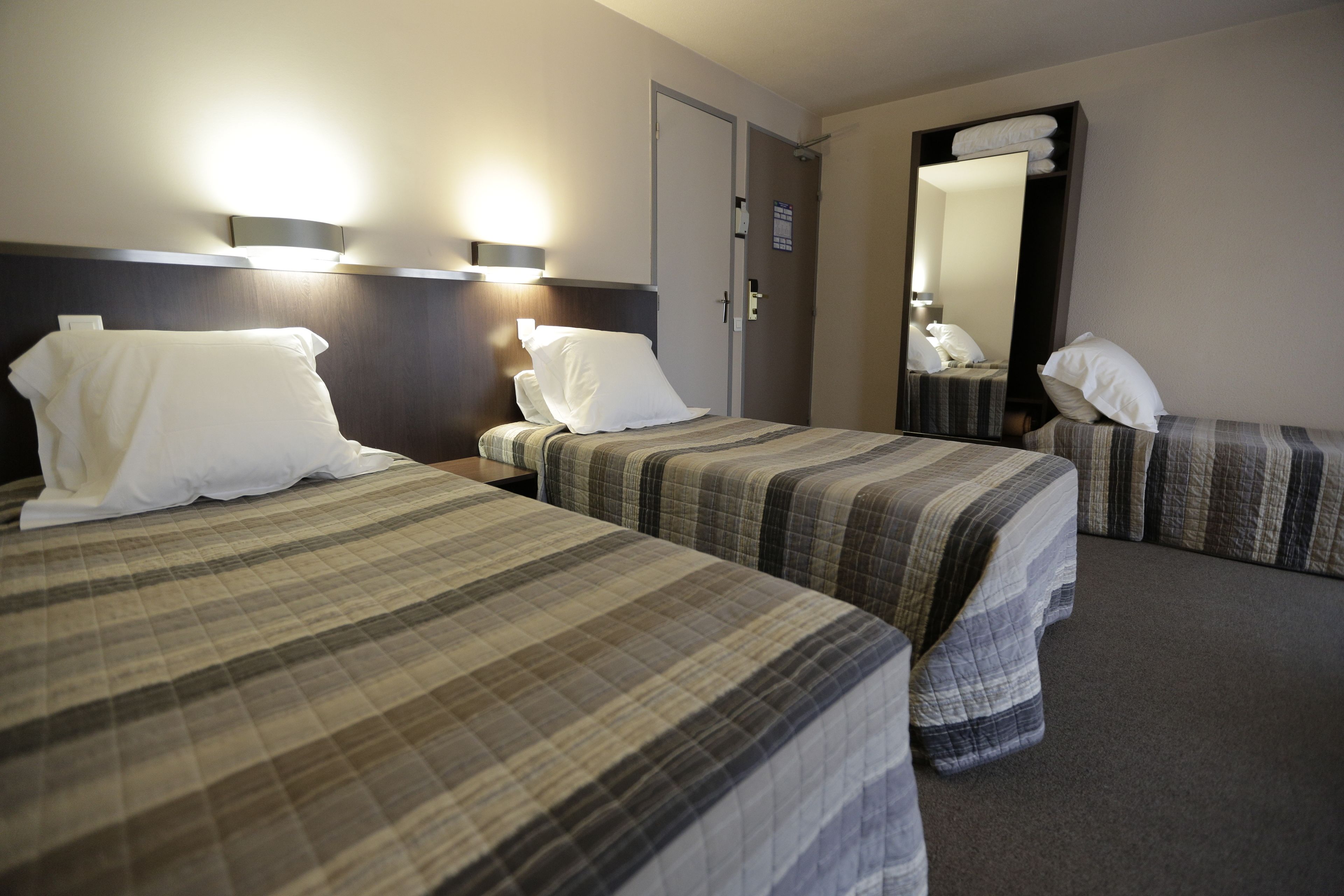 A hotel room with two beds, each with a plaid bedspread, a nightstand with a lamp, and a large mirror on the wall.
