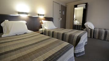 A hotel room with two beds, each with a plaid bedspread, a nightstand with a lamp, and a large mirror on the wall.