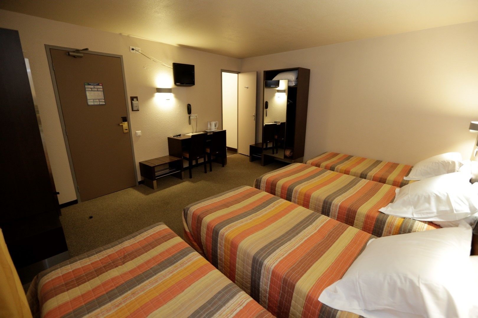 Une chambre d’hôtel avec trois lits, un bureau et un miroir.