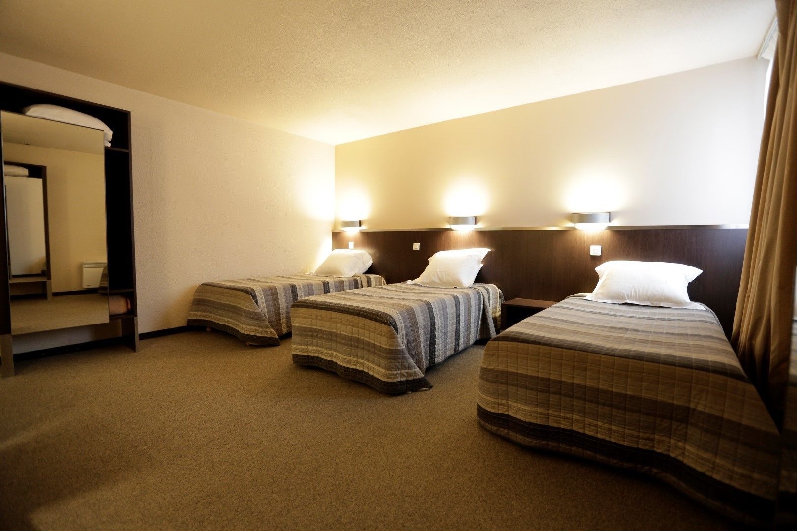A hotel room with three beds, each with a headboard and bedside lamps.