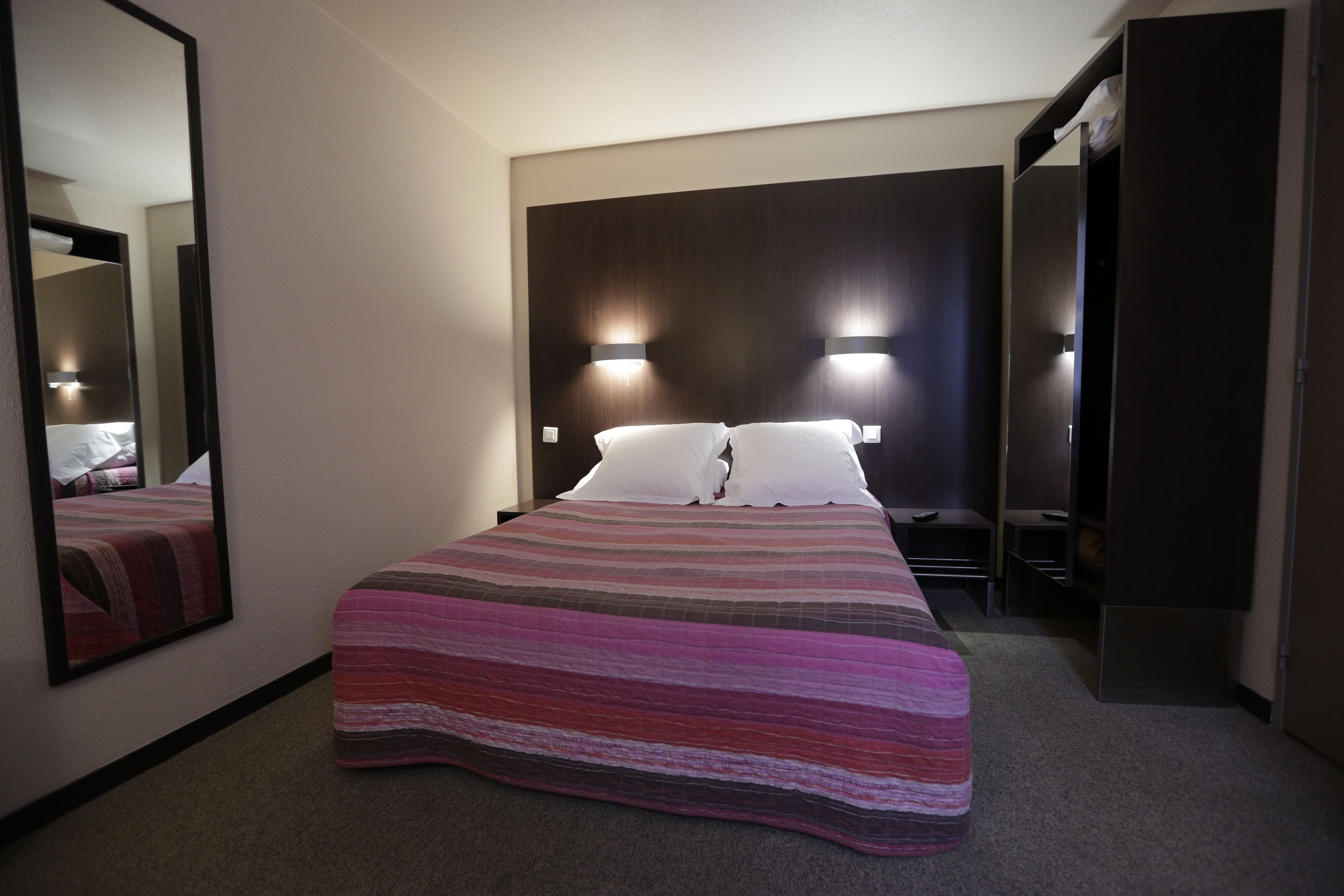 A hotel room with a large bed, two bedside lamps, a wardrobe, and a mirror.