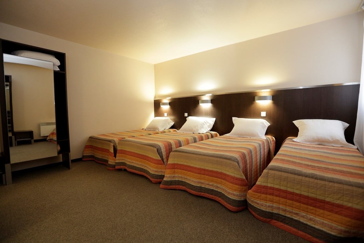 Een hotelkamer met drie bedden, elk voorzien van gestreept beddengoed, een grote spiegel en wandlampen.
