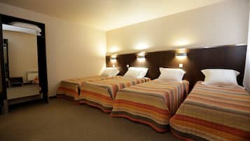 A hotel room with three beds, each with striped bedding, a large mirror, and wall-mounted lights.