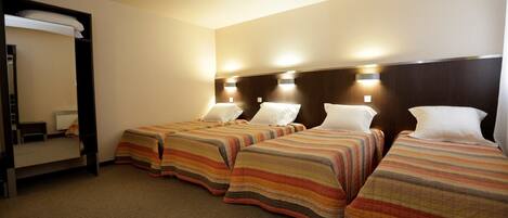 Habitación de hotel con tres camas, cada una con ropa de cama a rayas, un espejo grande y lámparas fijadas a la pared.