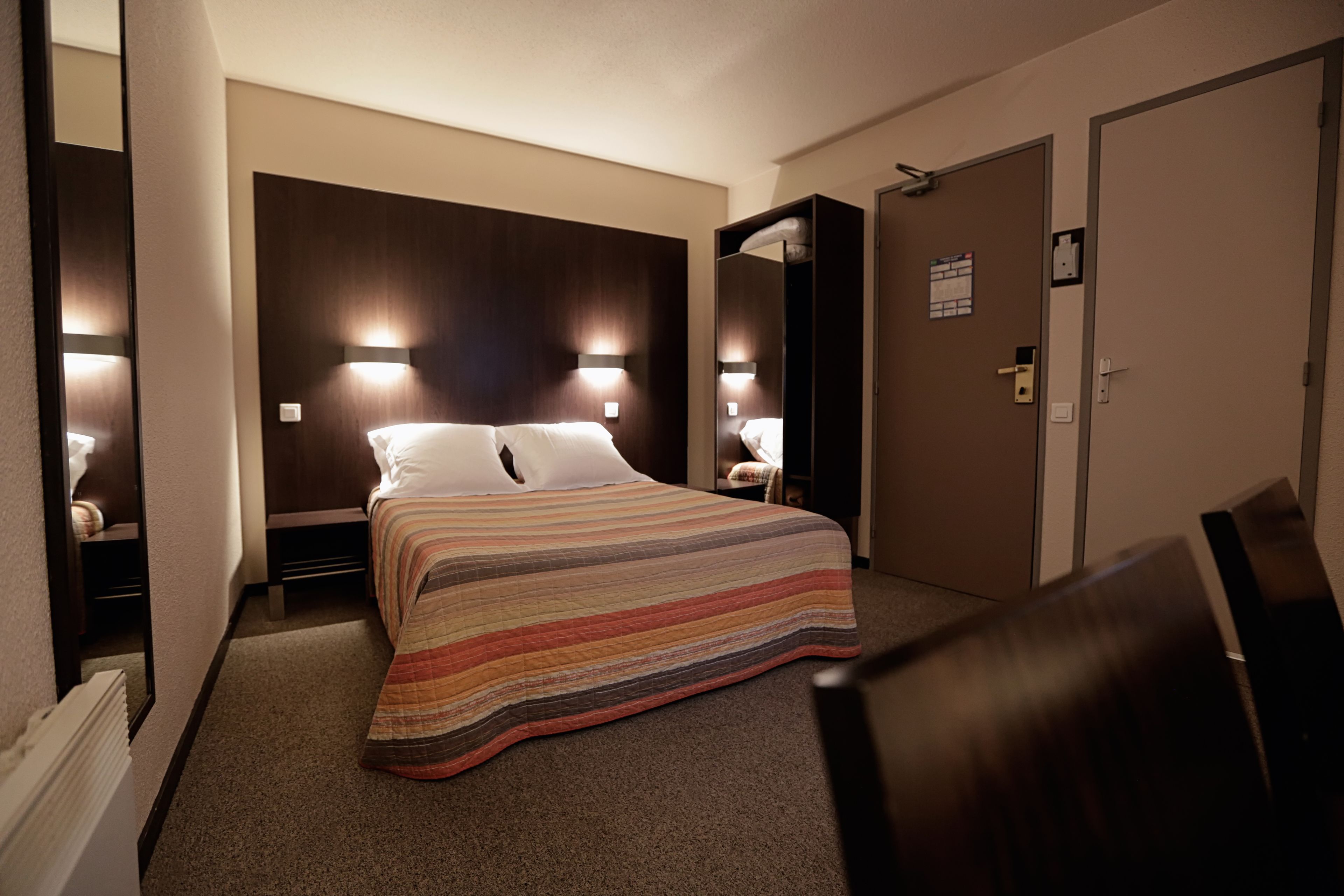 A hotel room with a large bed, two bedside tables, a nightstand, a mirror, and a door.