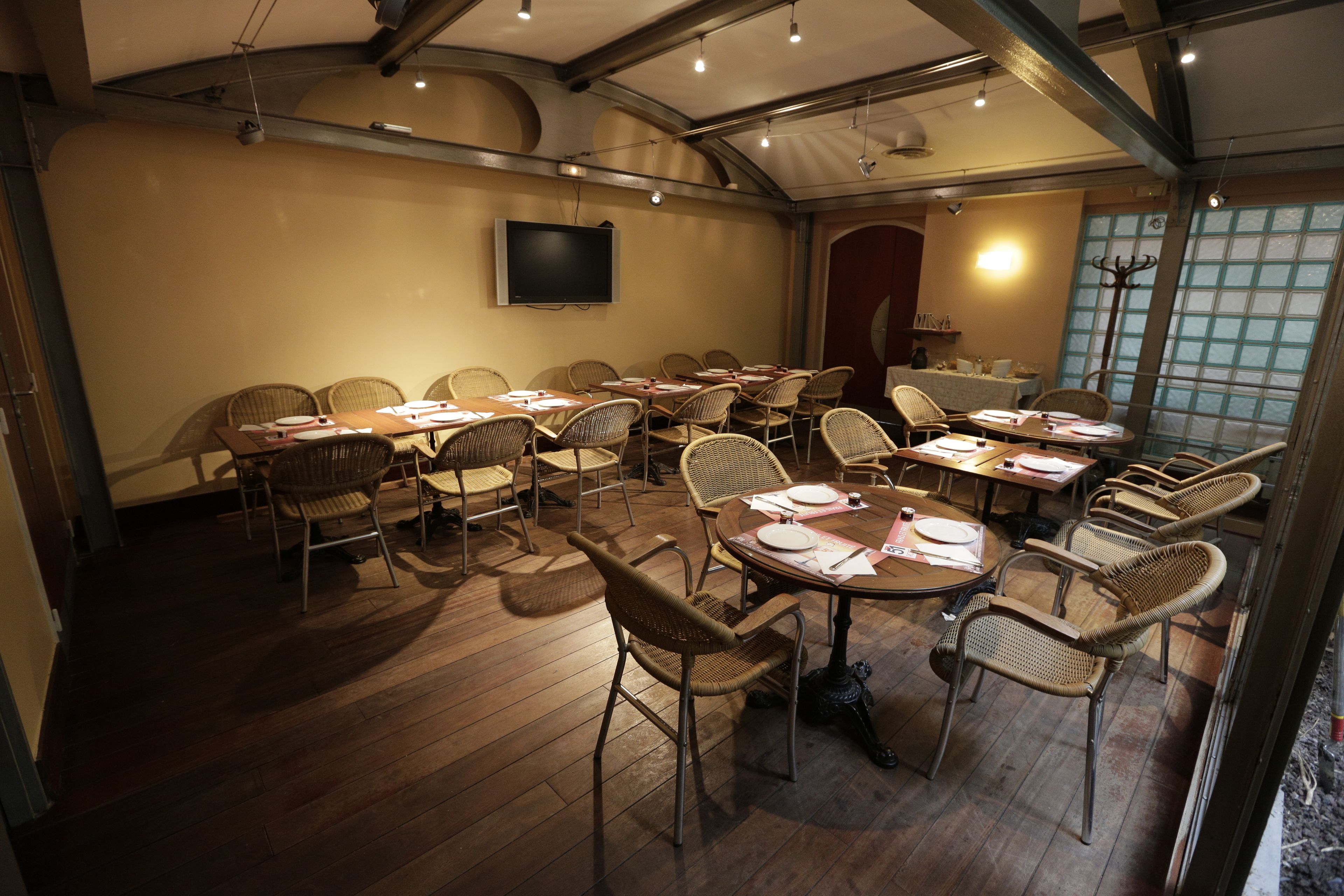 A conference room with multiple tables and chairs, a flat-screen TV mounted on the wall, and a large window with a view of the outside.