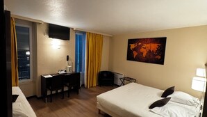 A hotel room with a bed, a desk, a chair, a TV mounted on the wall, and a small table with a remote control. - Hôtel Au Petit Caporal (Maisons-Alfort)