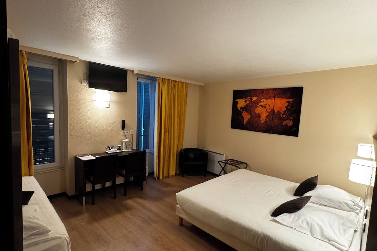 Een hotelkamer met een bed, een bureau, een stoel, een aan de muur bevestigde televisie en een klein tafeltje met een afstandsbediening.