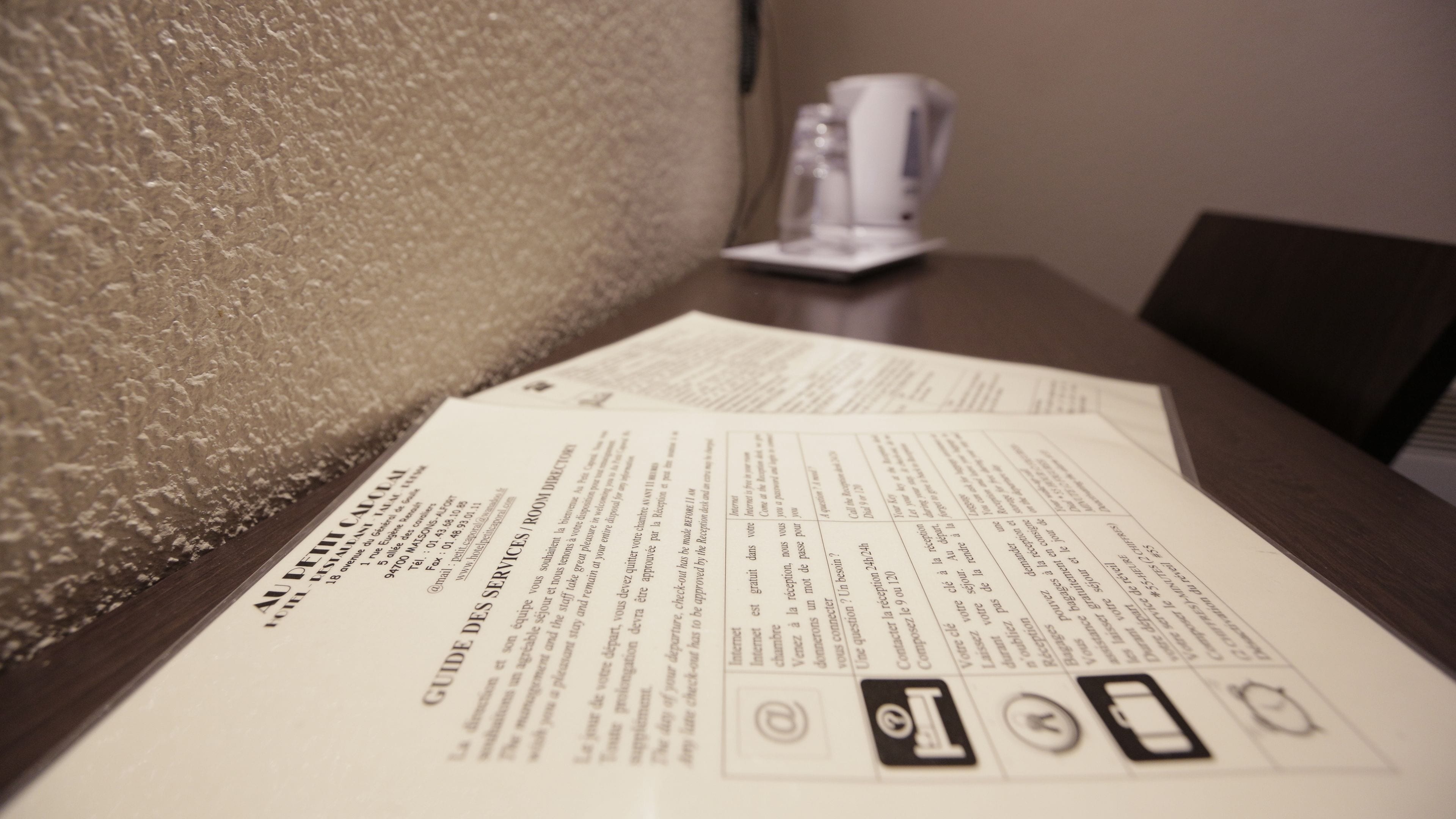 A hotel room with a textured wall and a table with a menu or informational pamphlet.