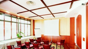 A conference room with a whiteboard, red chairs, a table, and a large window with blinds. - Hôtel Au Petit Caporal (Maisons-Alfort)