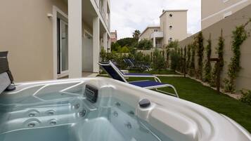 A hot tub with a view of a garden and a building in the background.