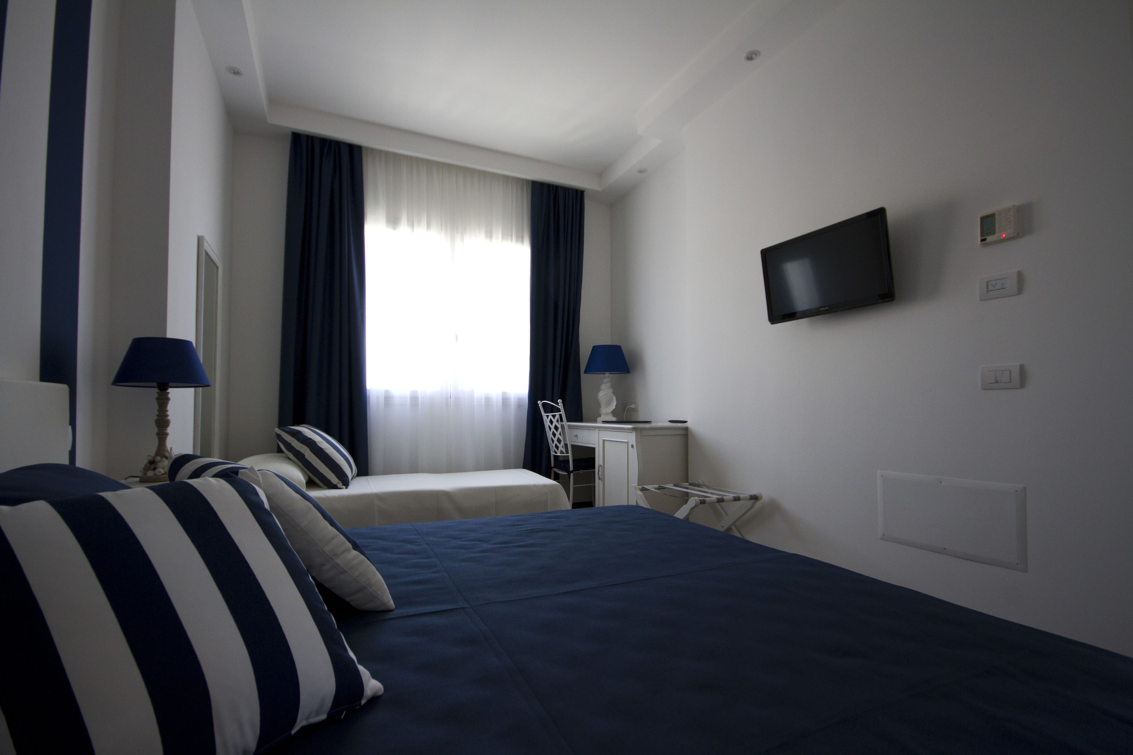 A hotel room with a bed, two bedside tables, a desk, a chair, a TV, and a window with curtains.