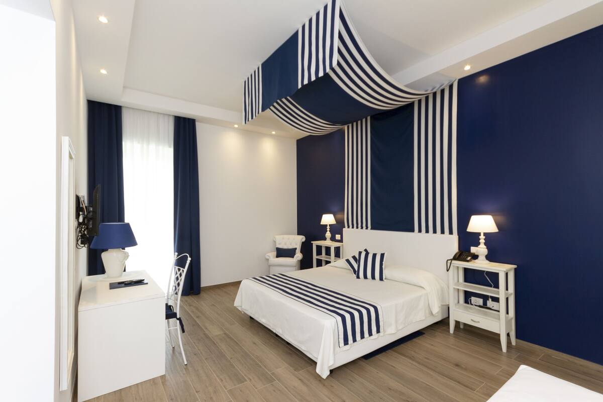 A modern bedroom with a large bed, bedside tables with lamps, a chair, and a desk with a lamp.
