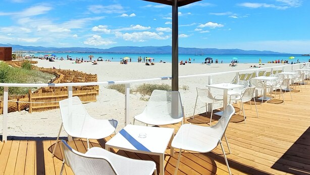 Een restaurant aan het strand met terras, met uitzicht op een zandstrand en de zee.