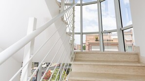 Een trap met witte leuningen die uitkomt op een balkon met grote ramen.