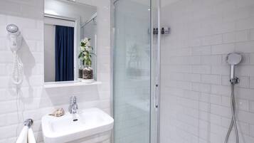 Un baño moderno con cabina de ducha de vidrio, un lavabo blanco y un secador de pelo montado en la pared.