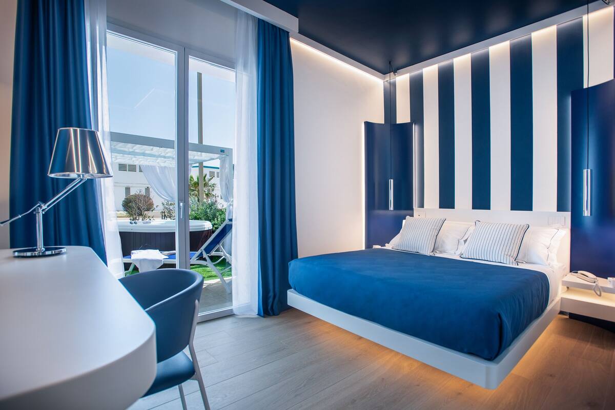 A modern hotel room with a large bed, a desk, and a view of the outdoors.