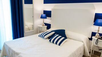 A neatly arranged bedroom with a large bed, two bedside tables, a mirror, and a blue-striped wall.