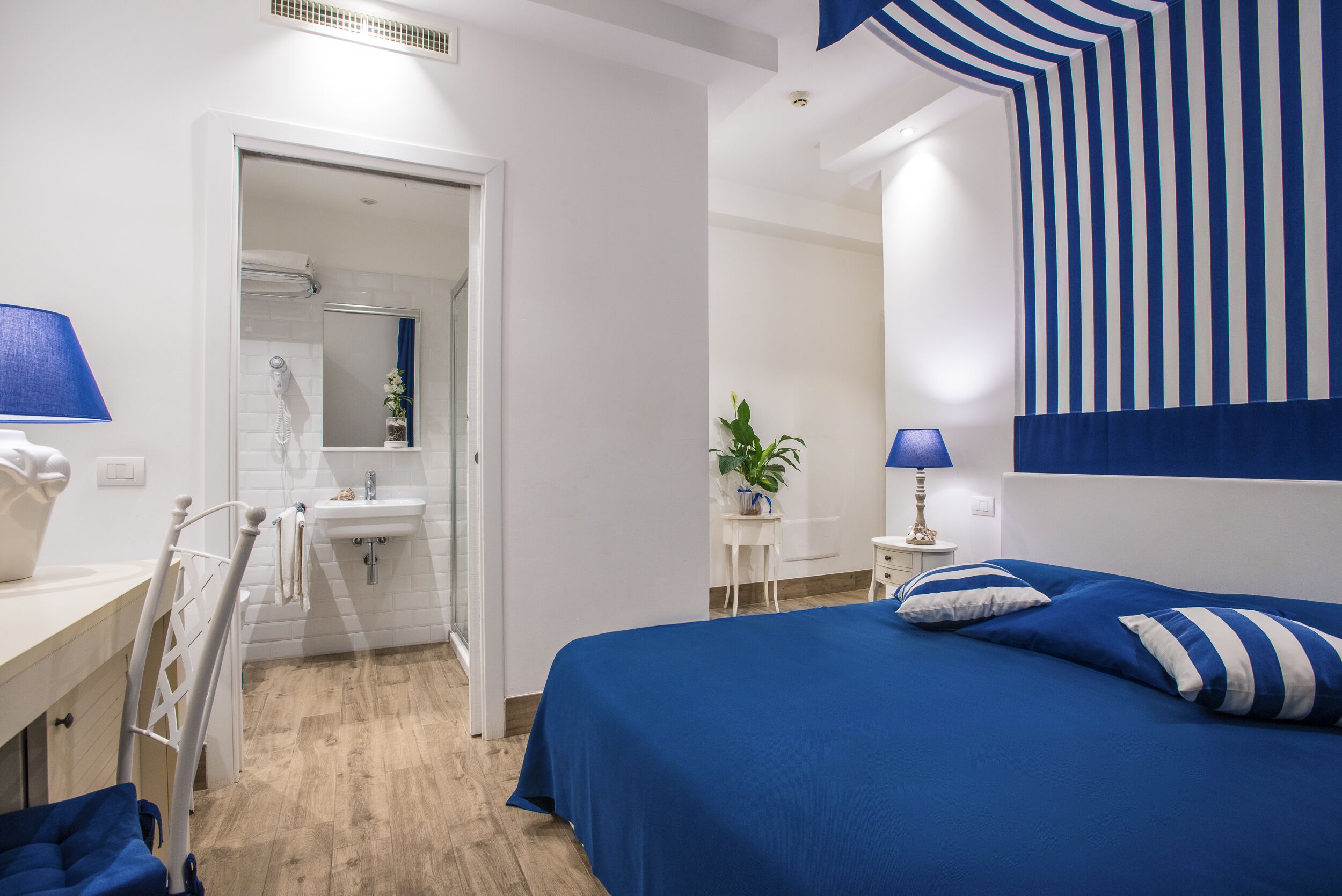 A bedroom with a bed, bedside table, lamp, and a view of the bathroom.