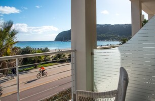 Un balcón con vista a una playa, una carretera con un ciclista y una silla.