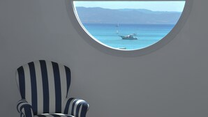 Een kamer met een rond raam met uitzicht op zee, een gestreept fauteuil en een zicht op boten op het water.