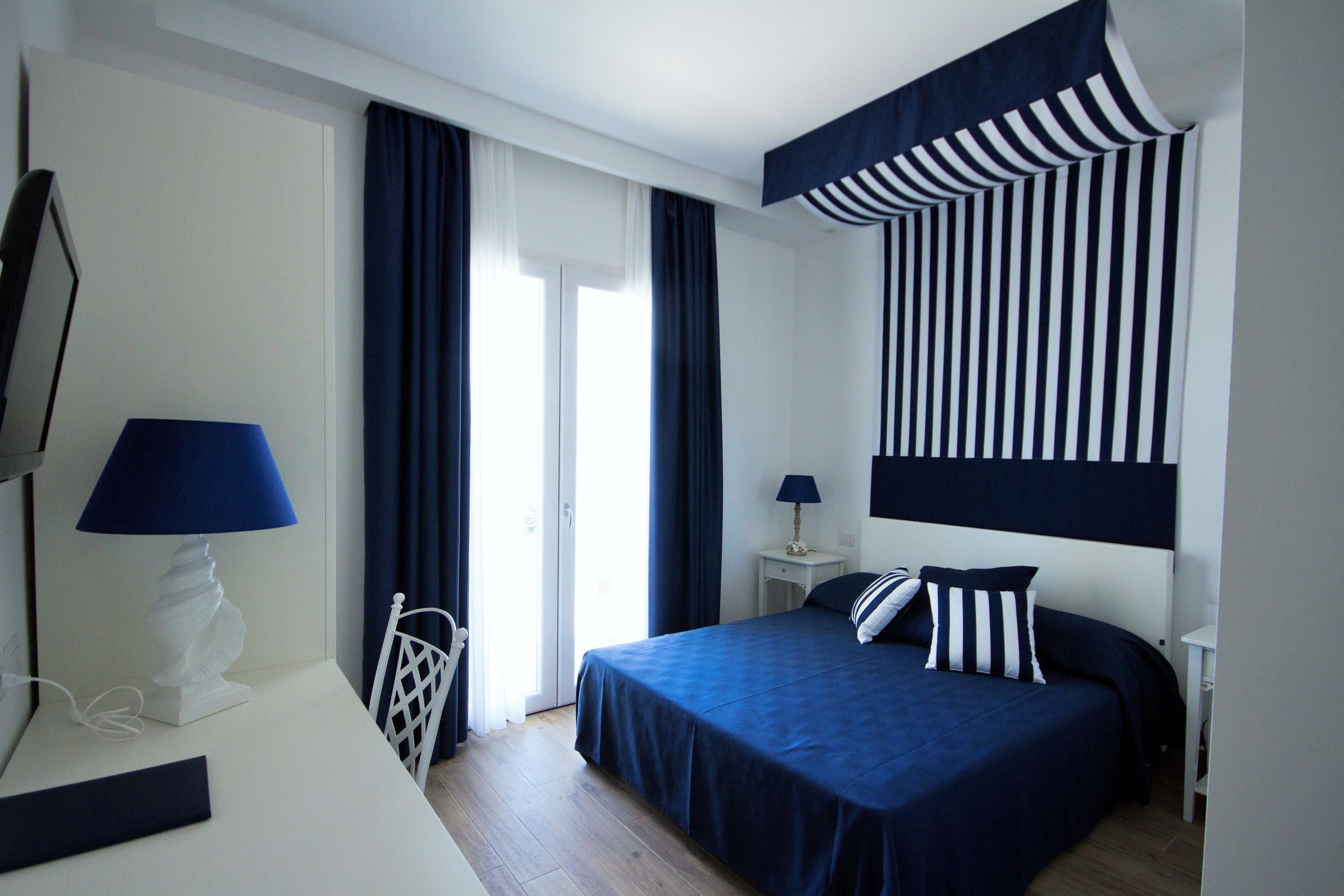 A hotel room with a bed, a desk with a lamp, a chair, a TV, and a window with curtains.