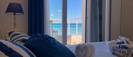 A hotel room with a bed, a lamp, a view of the beach, and a small table with a towel and a box.