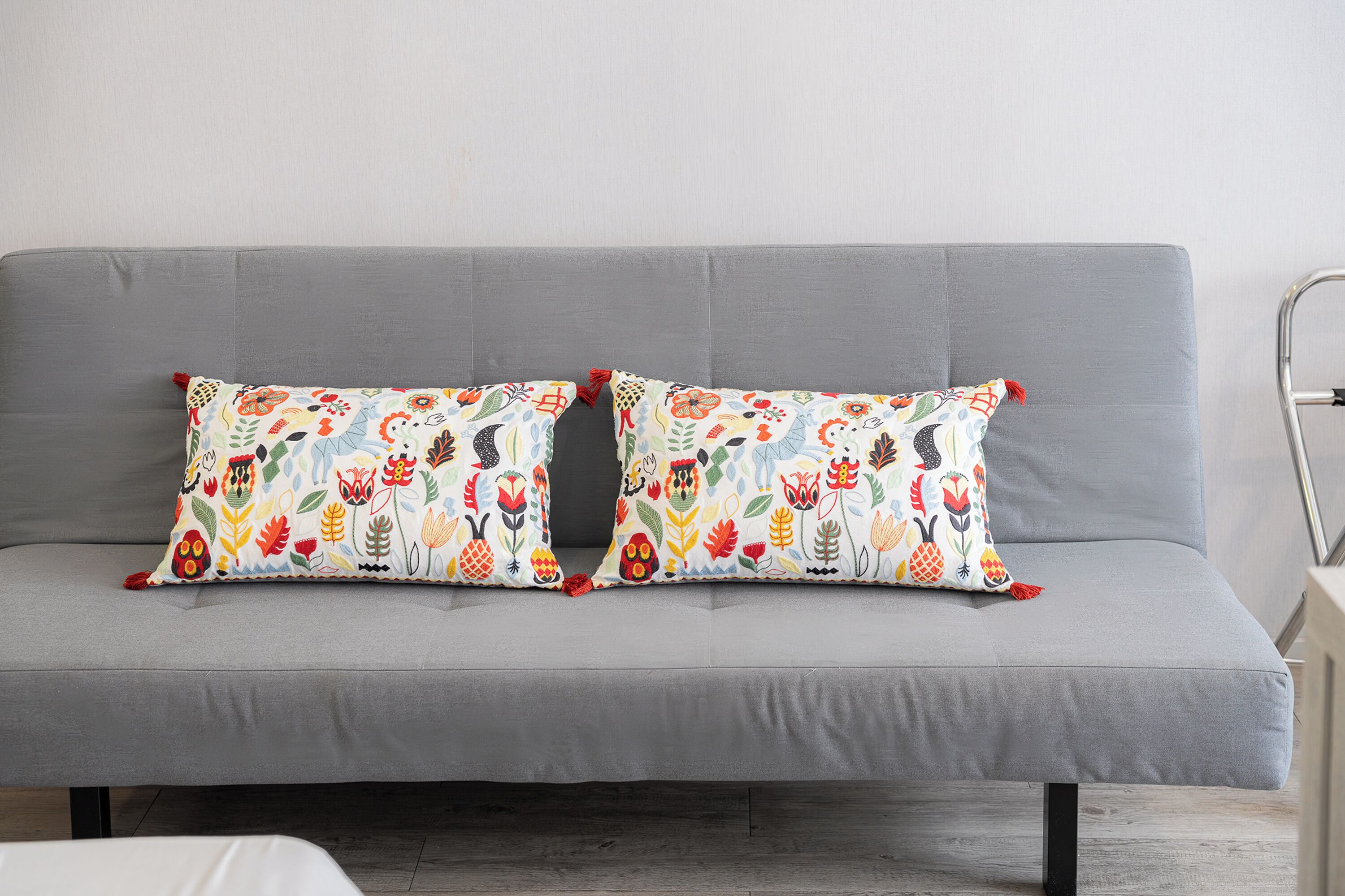 A grey sofa with two colorful pillows featuring floral and animal prints.