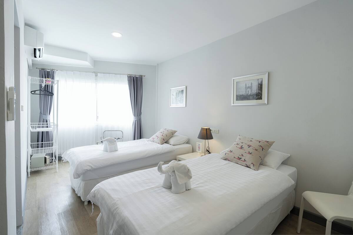 A hotel room with two beds, a small table, a chair, a lamp, and a wardrobe.