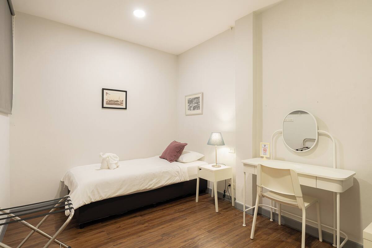 A bedroom with a bed, a desk, a chair, a mirror, and a wall-mounted shelf.