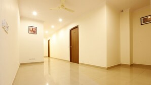 A spacious, well-lit hallway with a polished floor, a ceiling fan, and a door with a number plate. - Airport Hotel Chanakya (New Delhi)