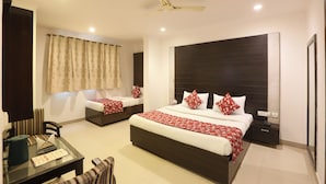 A hotel room with a large bed, a smaller bed, a desk with a chair, a ceiling fan, and a window with curtains. - Airport Hotel Chanakya (New Delhi)