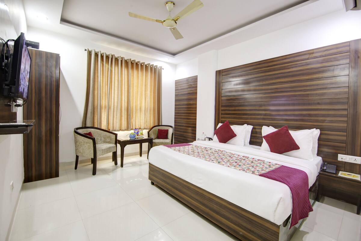 A hotel room with a large bed, a desk, a chair, a ceiling fan, and curtains.