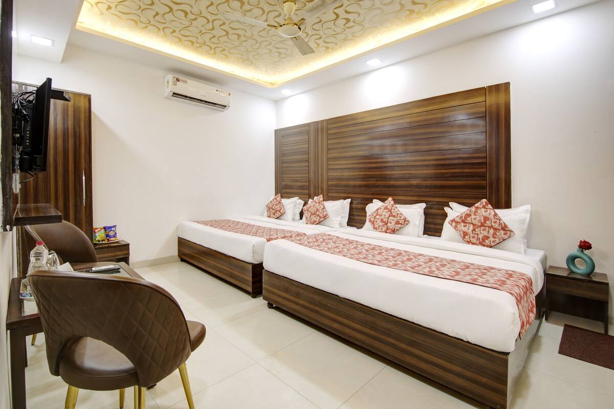 A hotel room with two beds, a desk, a chair, a TV, and an air conditioning unit.