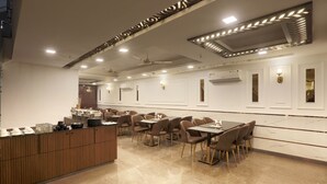 A modern dining area with a long counter, multiple tables, and chairs. - Airport Hotel Chanakya (New Delhi)
