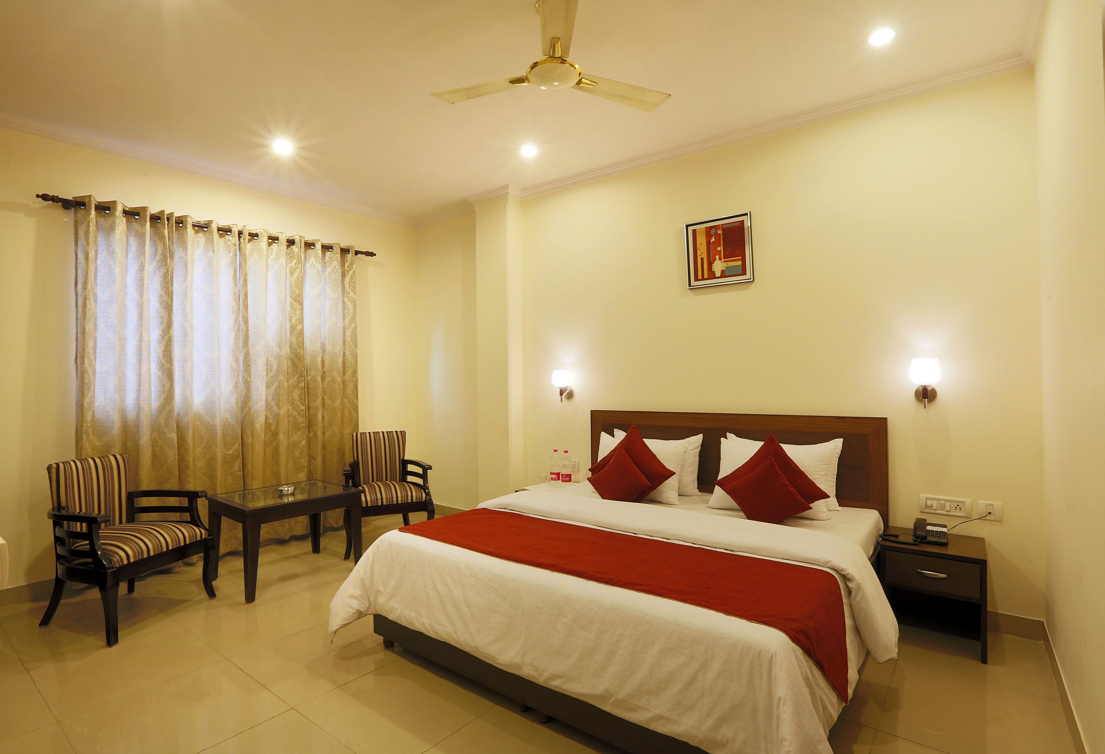 A hotel room with a large bed, two armchairs, a small table, a nightstand, and a ceiling fan.