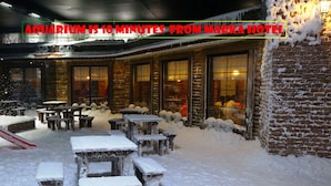 Een terras met tafels en banken bedekt met sneeuw, een bakstenen muur en een gebouw met grote ramen op de achtergrond.