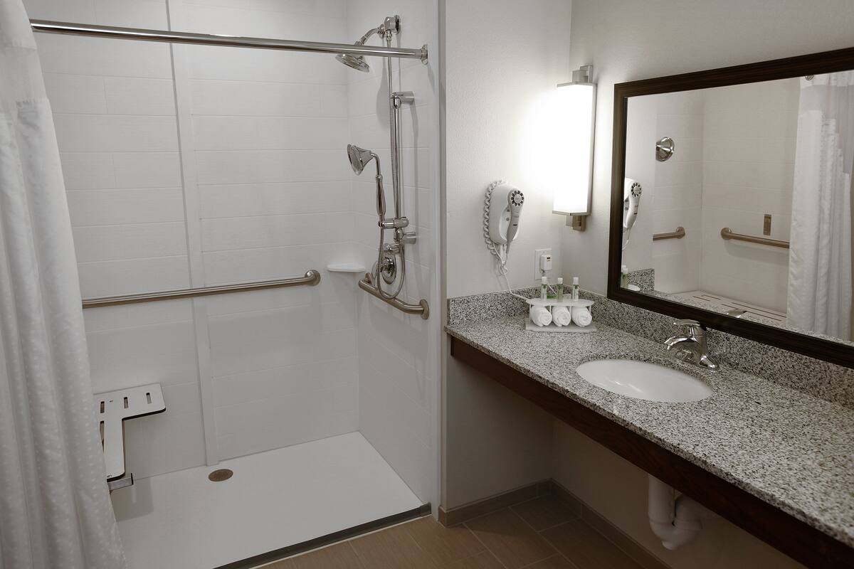 A bathroom with a shower, a sink, a mirror, and a towel rack.