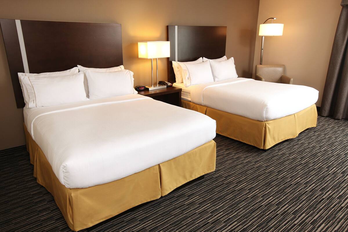 A hotel room with two beds, a nightstand with a lamp, and a chair.
