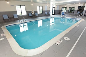 Una piscina interior con agua cristalina, señales de seguridad y sillas de descanso.