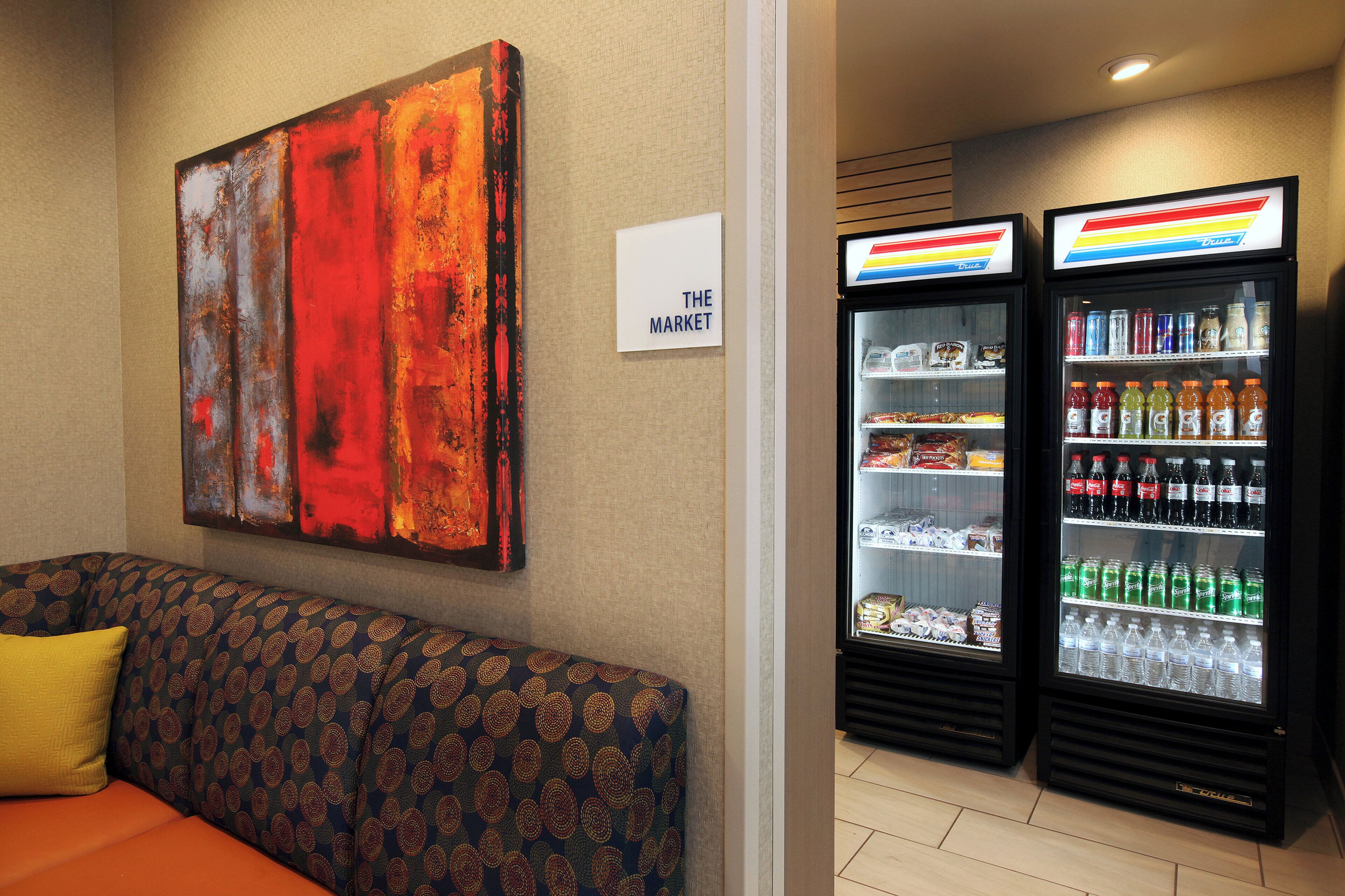 A hotel room with a sofa, a painting on the wall, and two beverage dispensers.