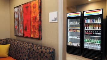 A hotel room with a sofa, a painting on the wall, and two beverage dispensers.