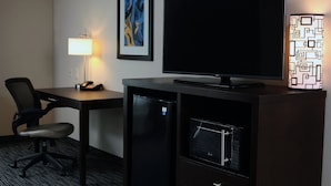 Ein Hotelzimmer mit Schreibtisch, Stuhl, Fernseher, Kühlschrank und Lampe.